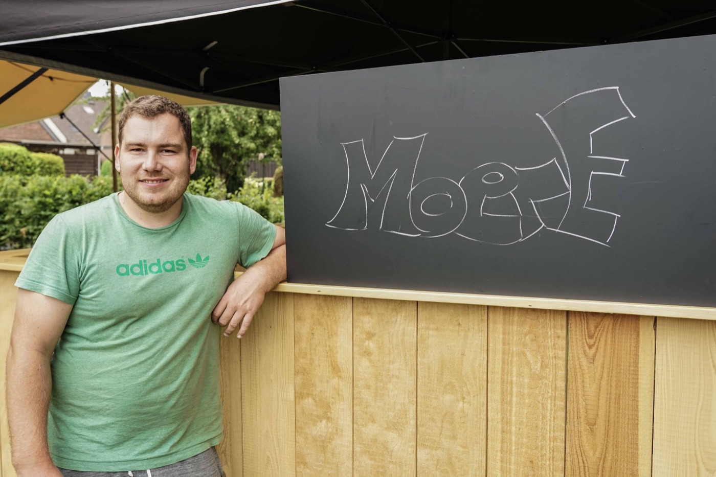 Der MOERE-Gründer lehnt an einem Holzstand mit dem auf eine Tafel gezeichneten MOERE-Schriftzug